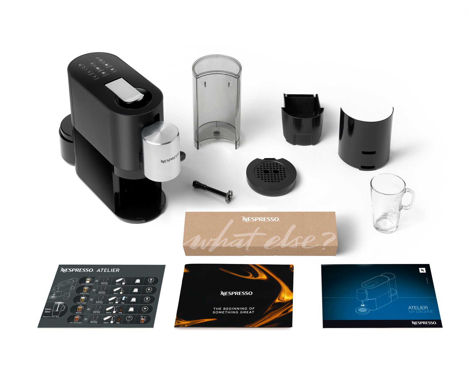 Siyah Nespresso Atelier makinesi, aksesuarlar, talimatlar ve beyaz bir yüzeyde bir fincan.