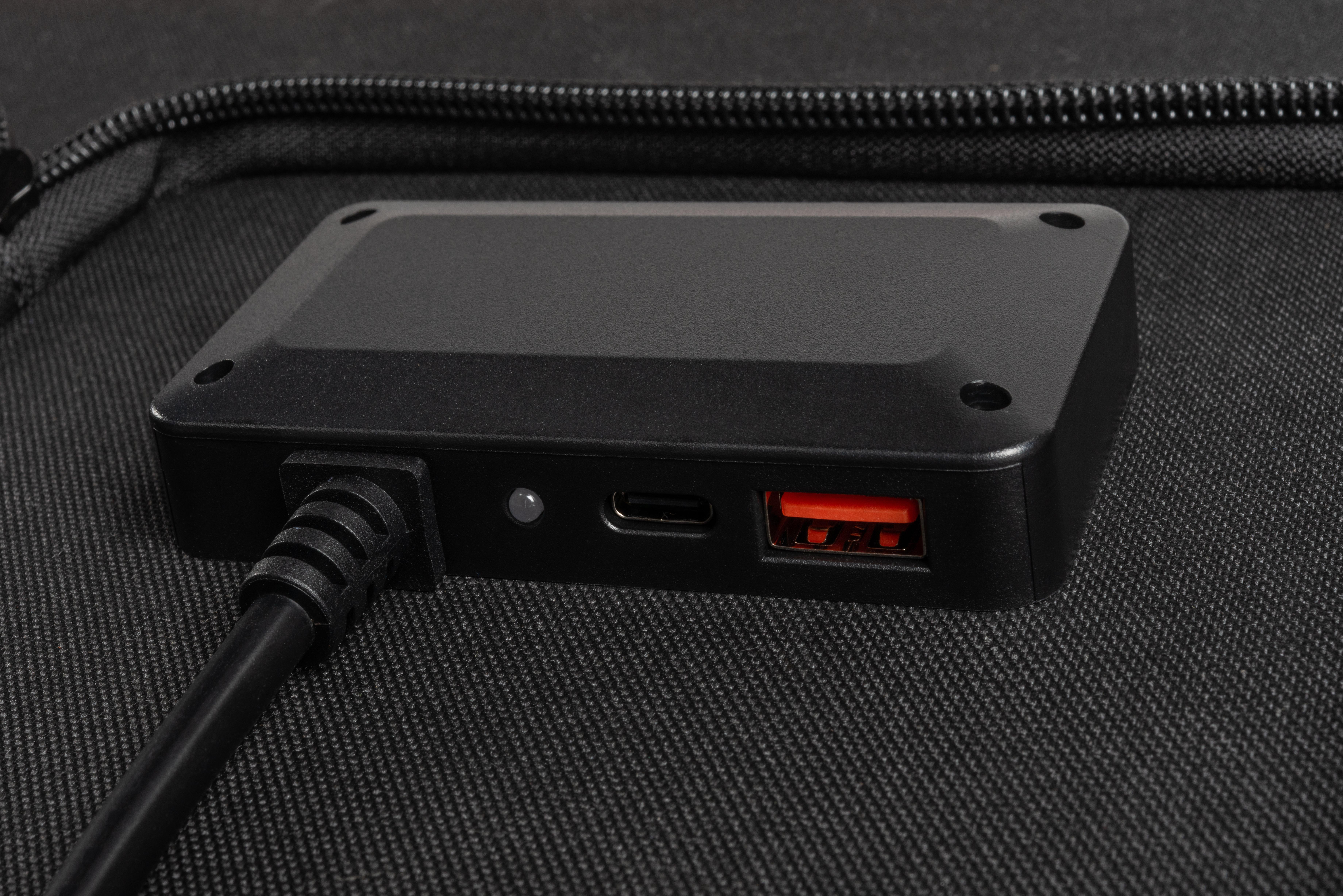 Schwarzer Lade-Hub. Er hat einen USB- und USB-C-Anschluss und liegt auf schwarzem Grund.