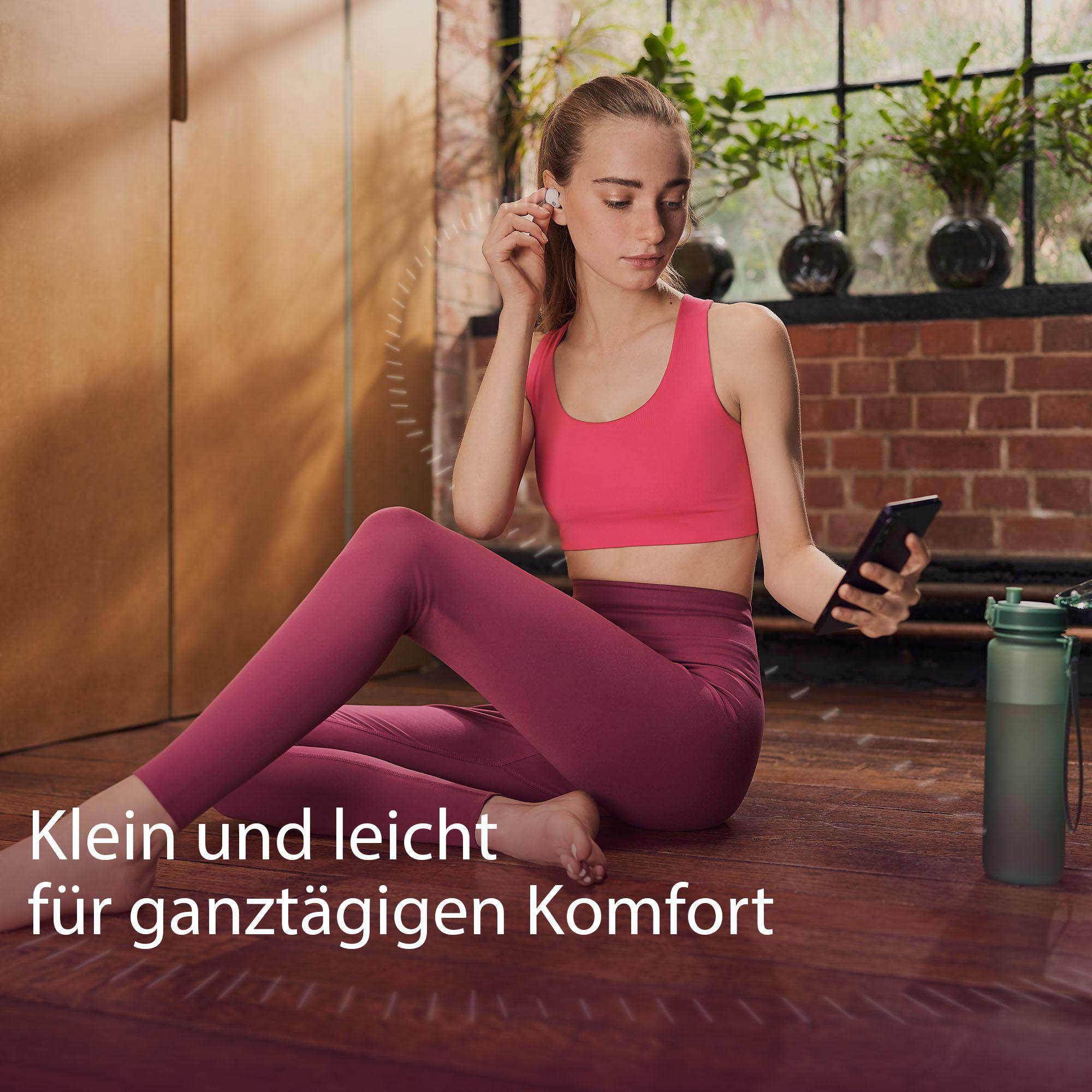 Frau mit Ohrhörern, die ein Telefon hält, sitzt auf einem Holzboden.