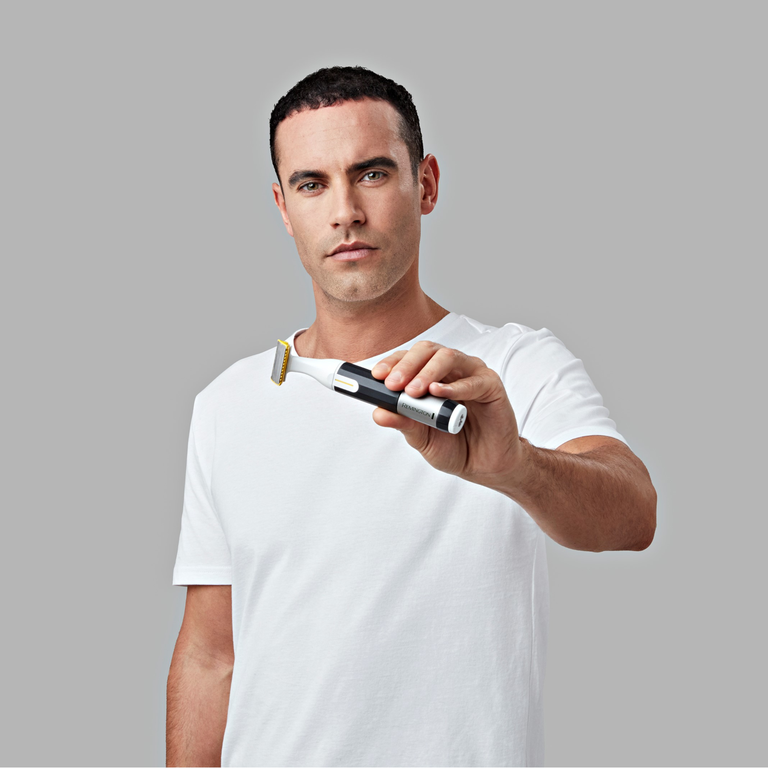 A man in a white shirt holds a beard trimmer, looking directly at the viewer.