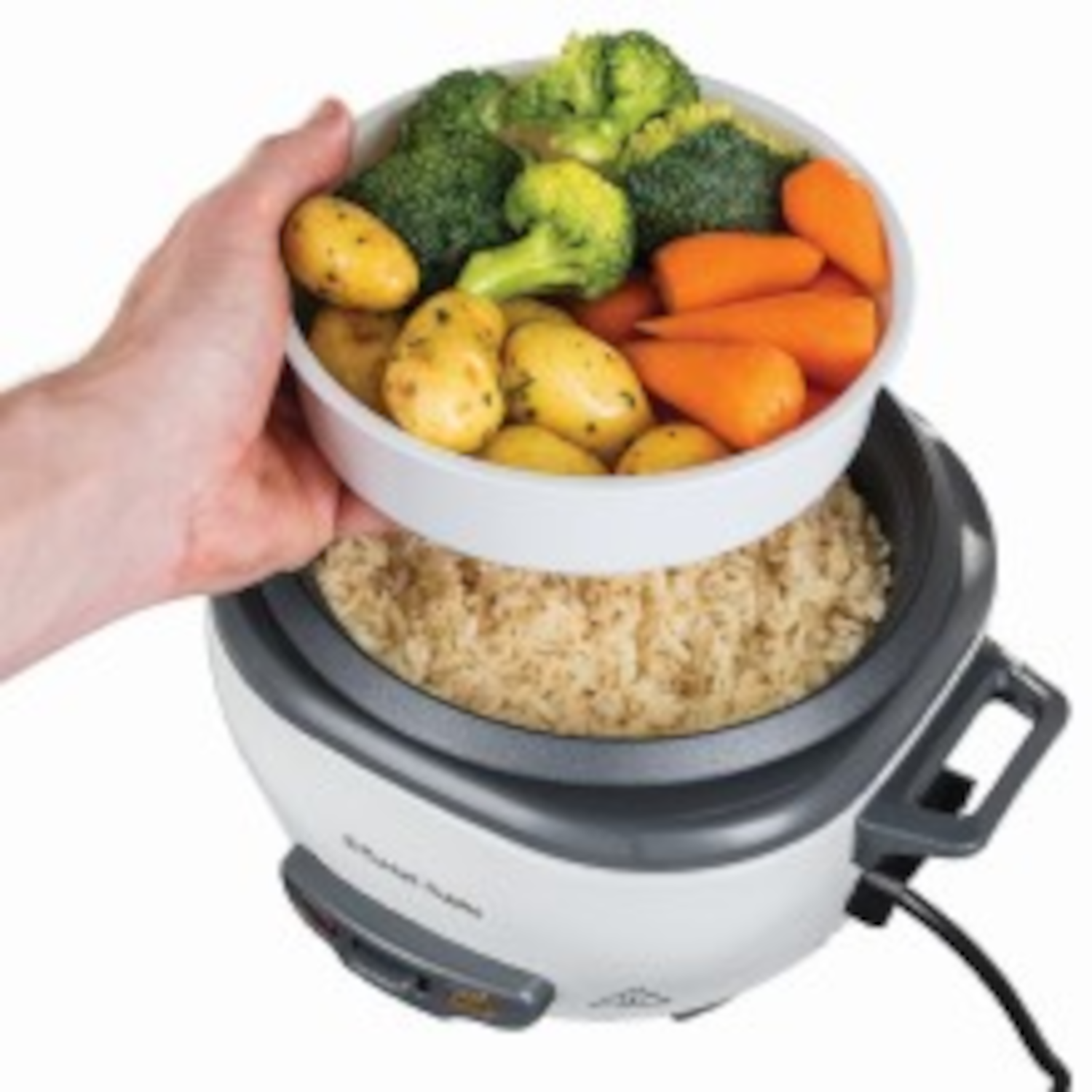 A person holding a bowl of cooked vegetables above a rice cooker with brown rice.