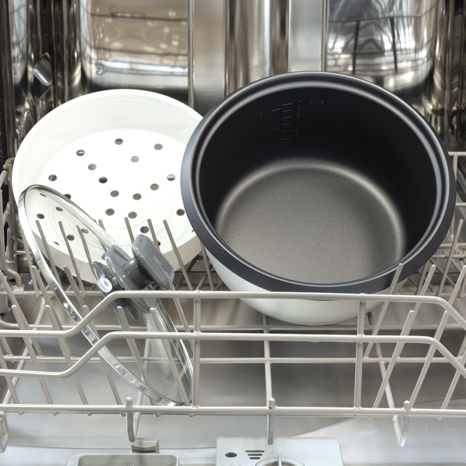 Inside a dishwasher: a rice cooker bowl, a steamer, and a glass lid on racks.