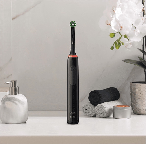 Brosse à dents électrique noire sur un comptoir blanc. Distributeur de savon, serviettes et une plante.