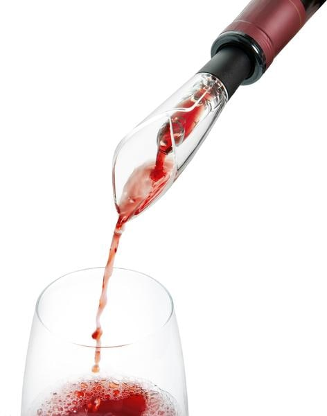 Un aérateur à vin verse du vin rouge dans un verre à vin clair, sur fond blanc.