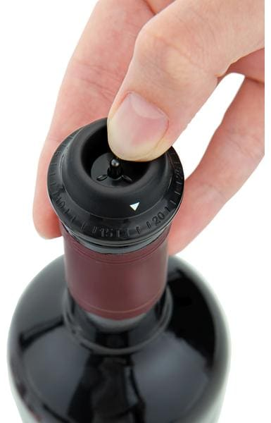 Main pressant un bouchon de vin noir dans une bouteille de vin.