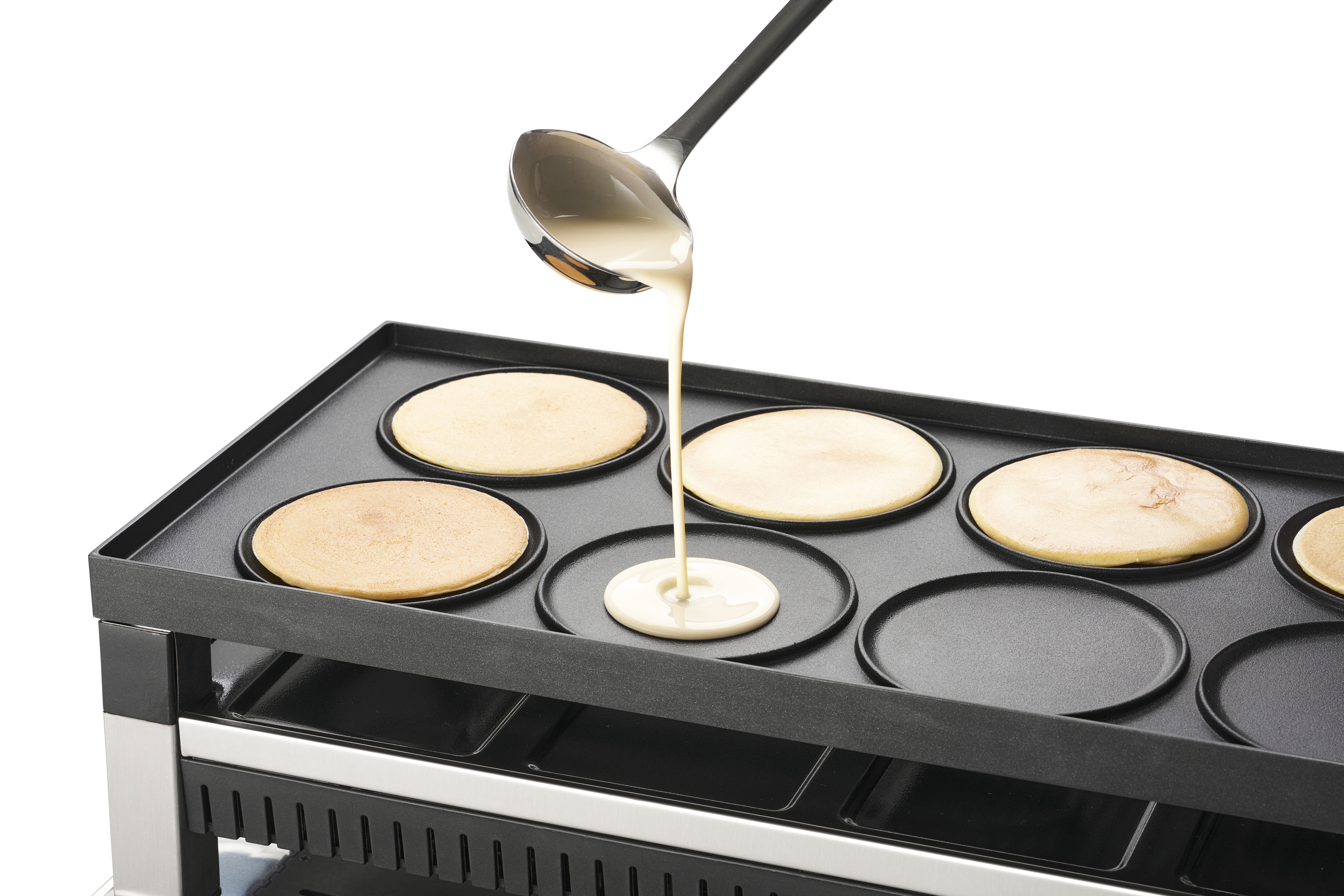 Pannenkoekenbeslag wordt op een bakplaat met cirkelvormige mallen gegoten. Een pannenkoek is al gaar.