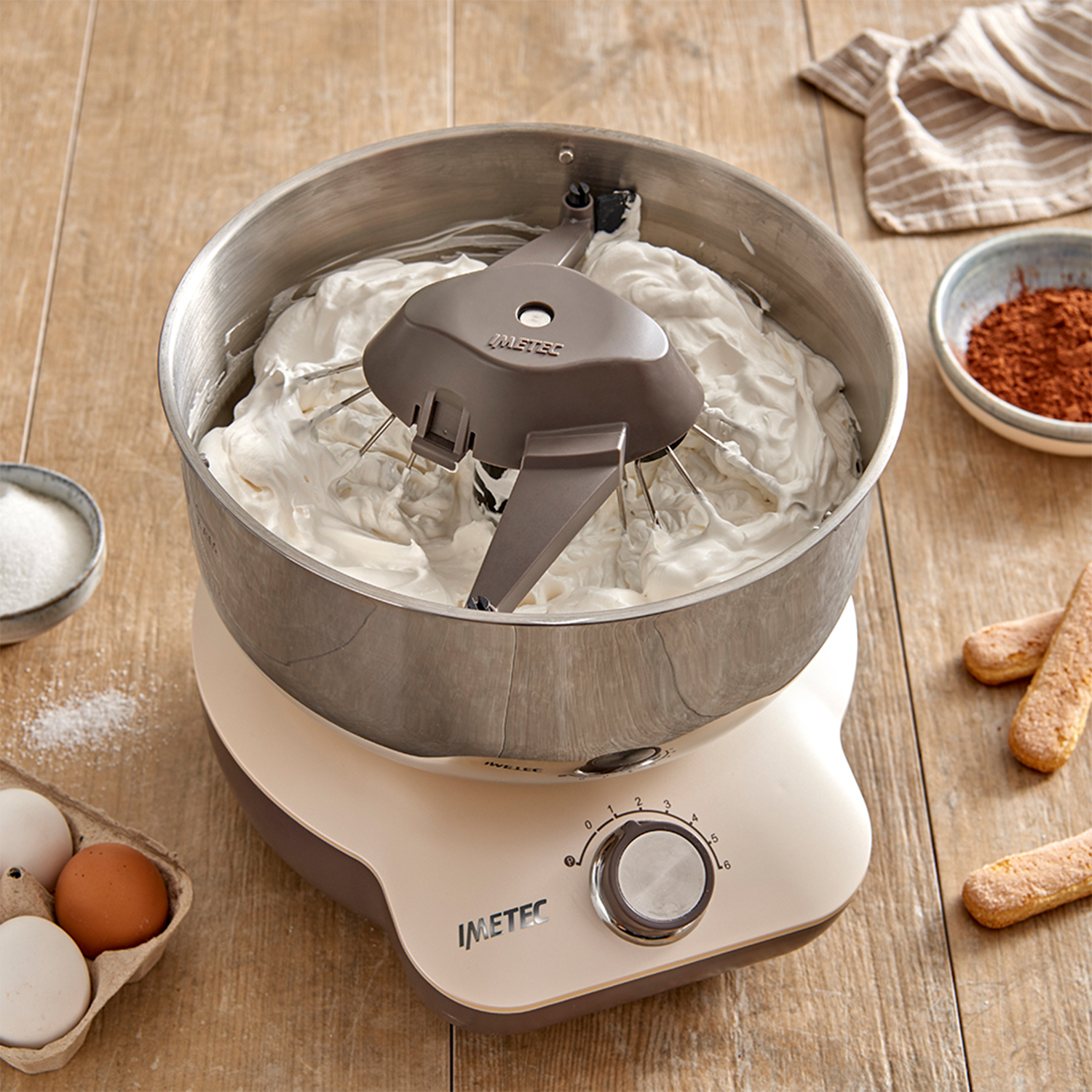 Un mixer a stand beige e acciaio inox con panna montata, con ingredienti intorno.