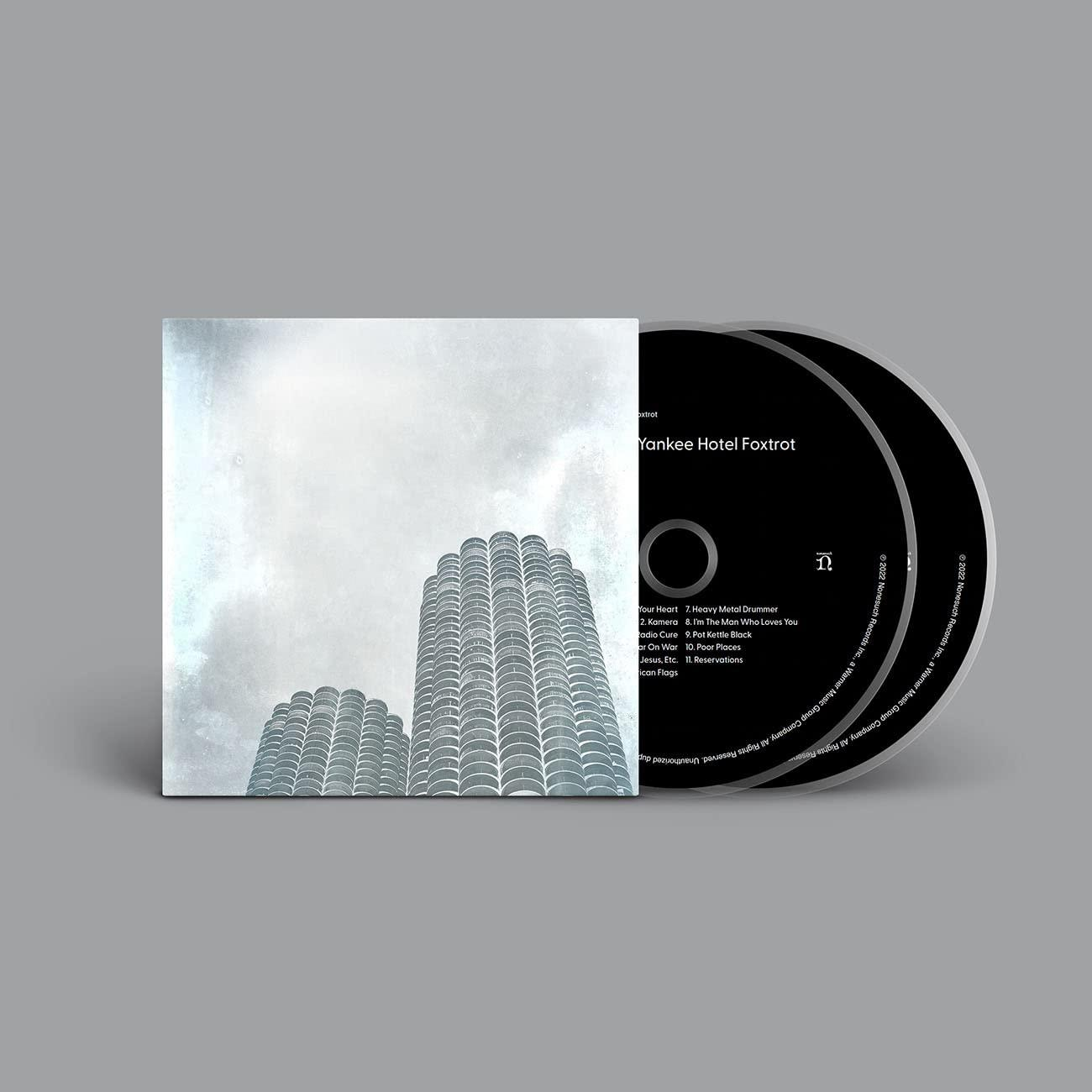 CD tok két CD-vel, albumborító városi felhőkarcolókkal, szürke égbolt háttérrel.