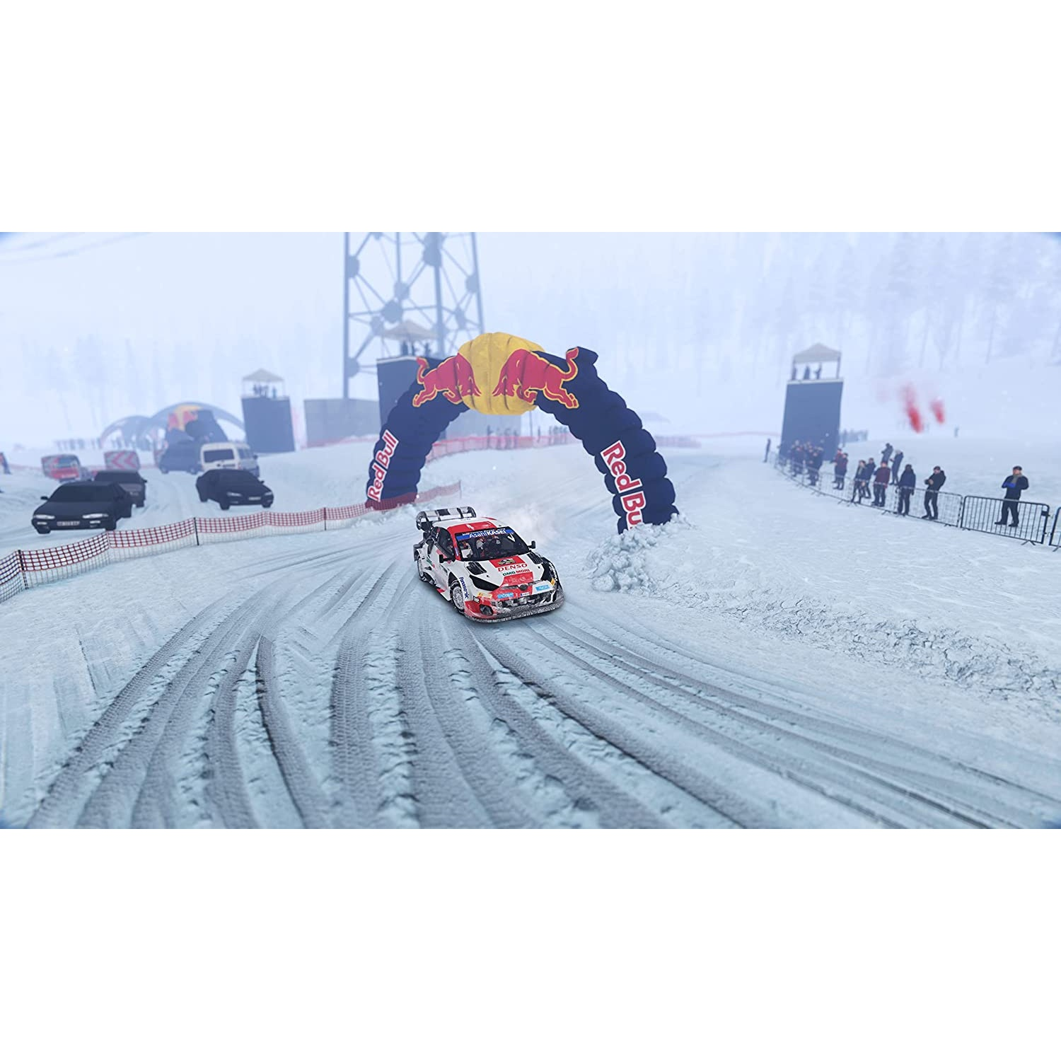 Un coche de rally compite en una pista nevada. Un arco de Red Bull está sobre la pista. Los espectadores son visibles.