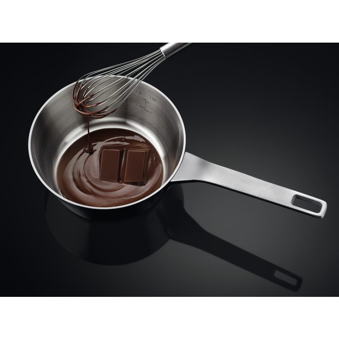 Chocolate derretido en una sartén con batidor. Fondo negro.