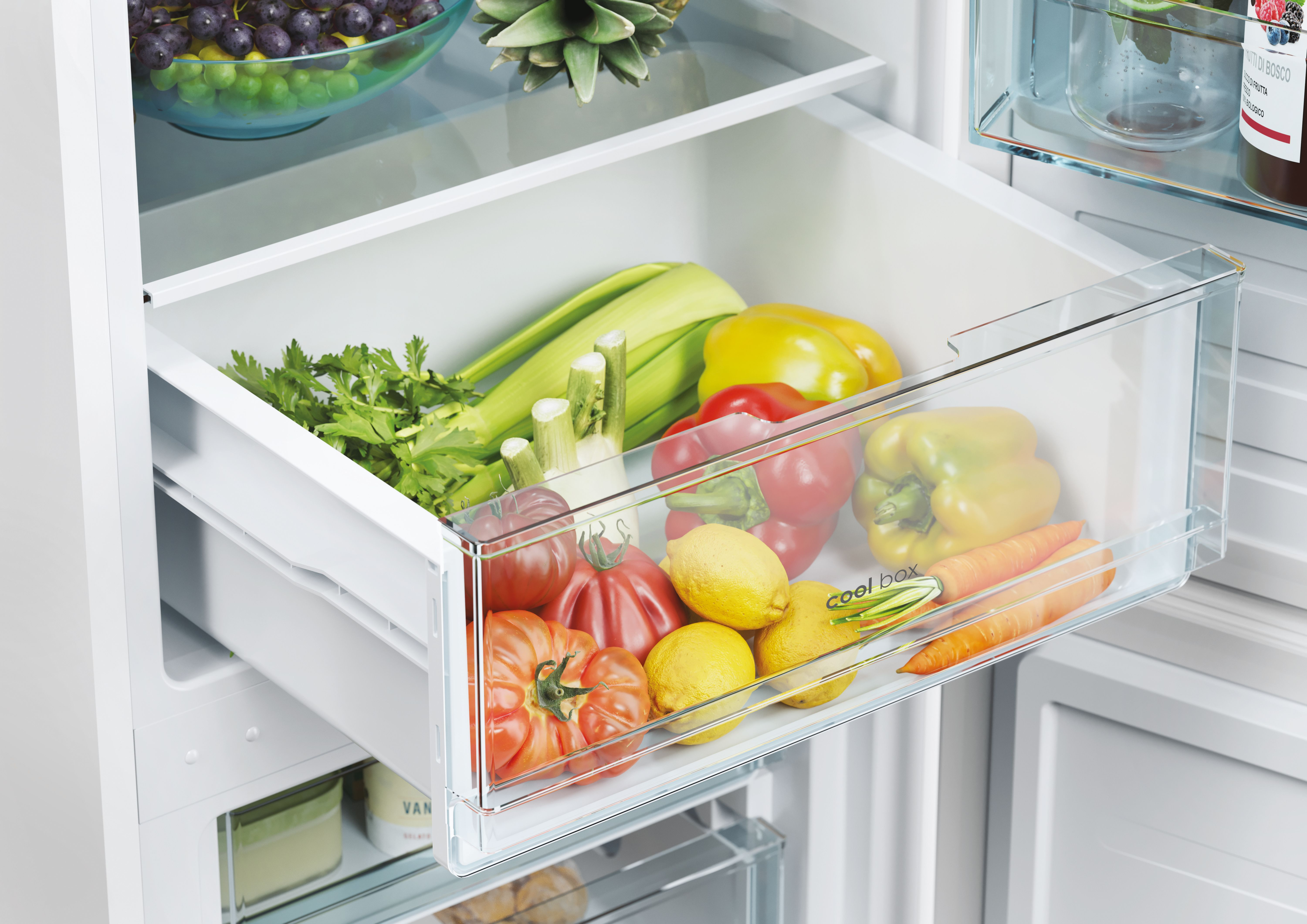 Un cajón de refrigerador lleno de verduras, incluyendo tomates, pimientos y zanahorias.