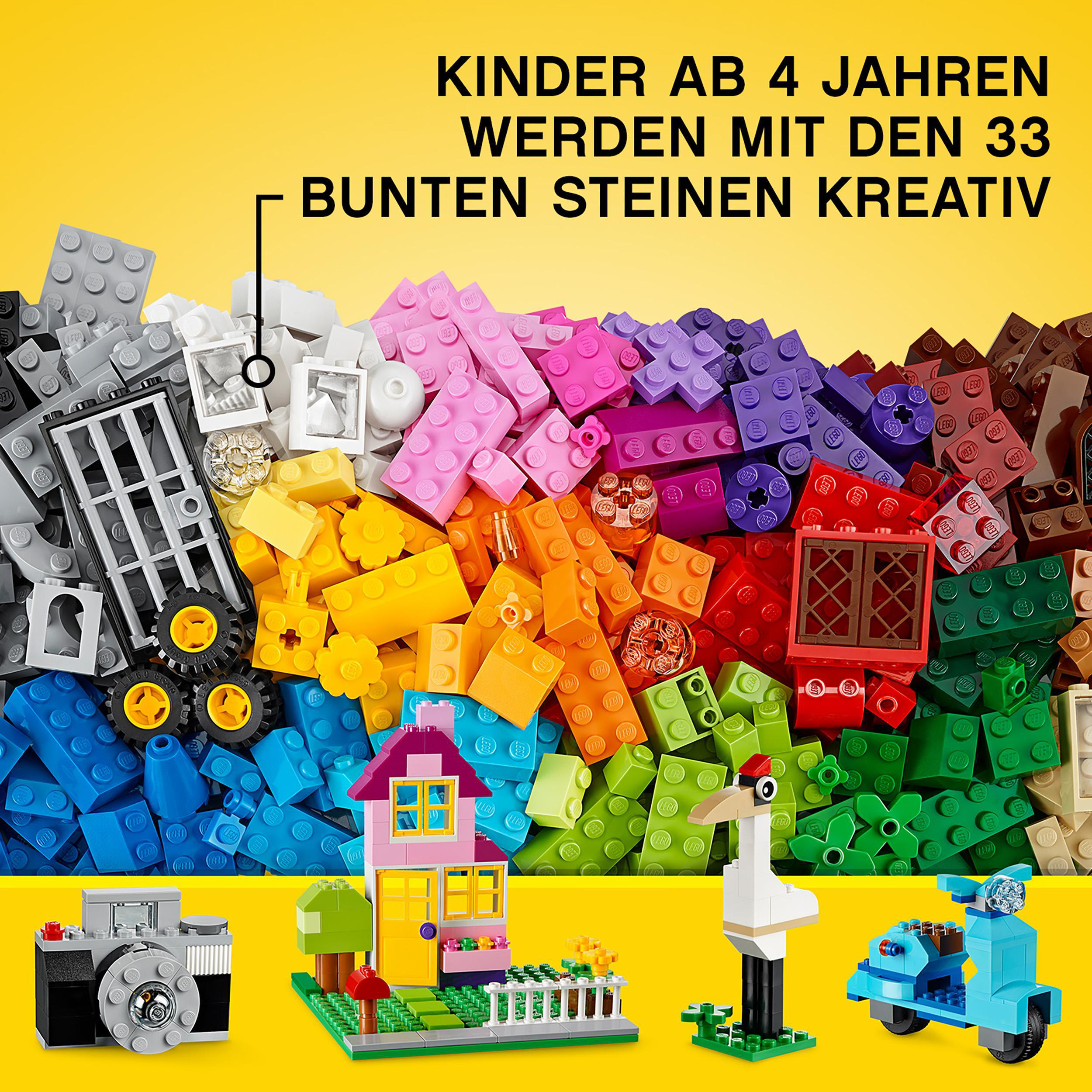 Eine Vielzahl bunter Lego-Steine ist ausgebreitet. Lego-Modelle eines Hauses, einer Kamera, eines Rollers und eines Storchs sind vorhanden.