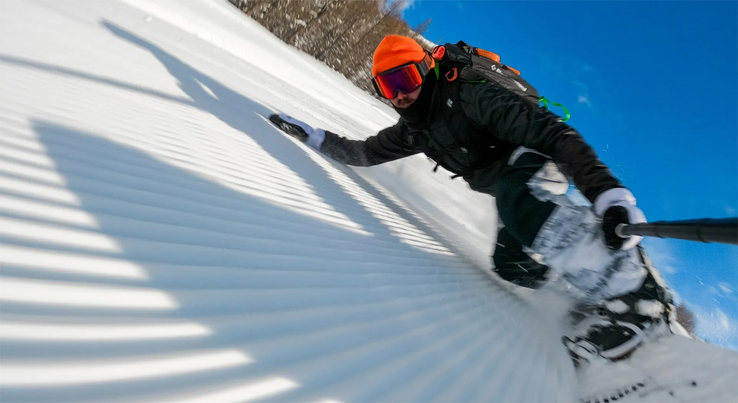 Un snowboardeur dévalant une pente enneigée par une journée ensoleillée. Le ciel est bleu.