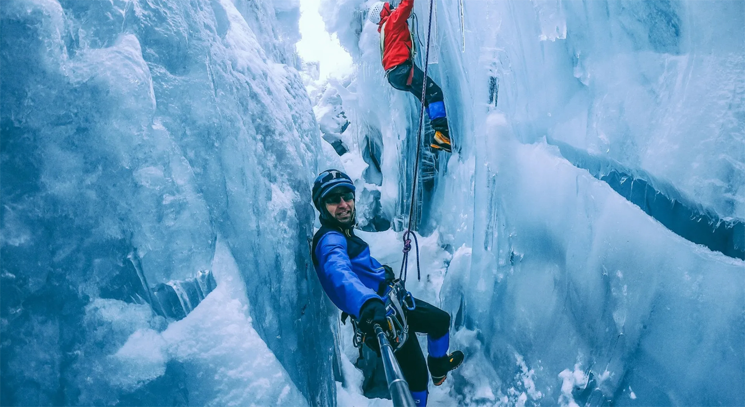 Deux personnes font de l'escalade sur glace dans une crevasse étroite. L'un prend un selfie.