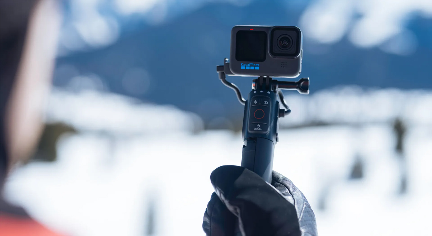 A person is holding a GoPro camera on a stick, snowy background.