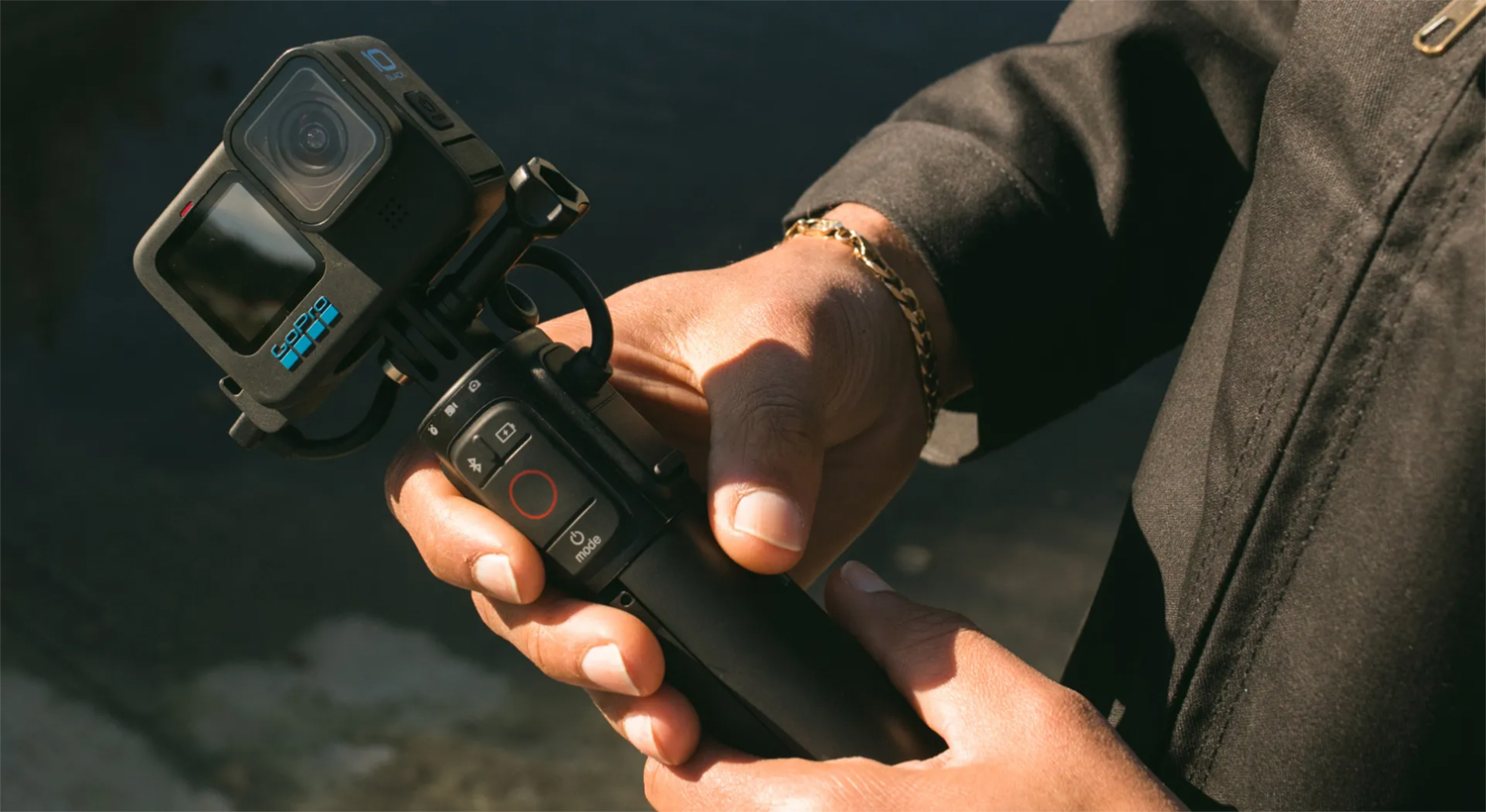 A person holding a black GoPro camera on a handle. The background is blurred.