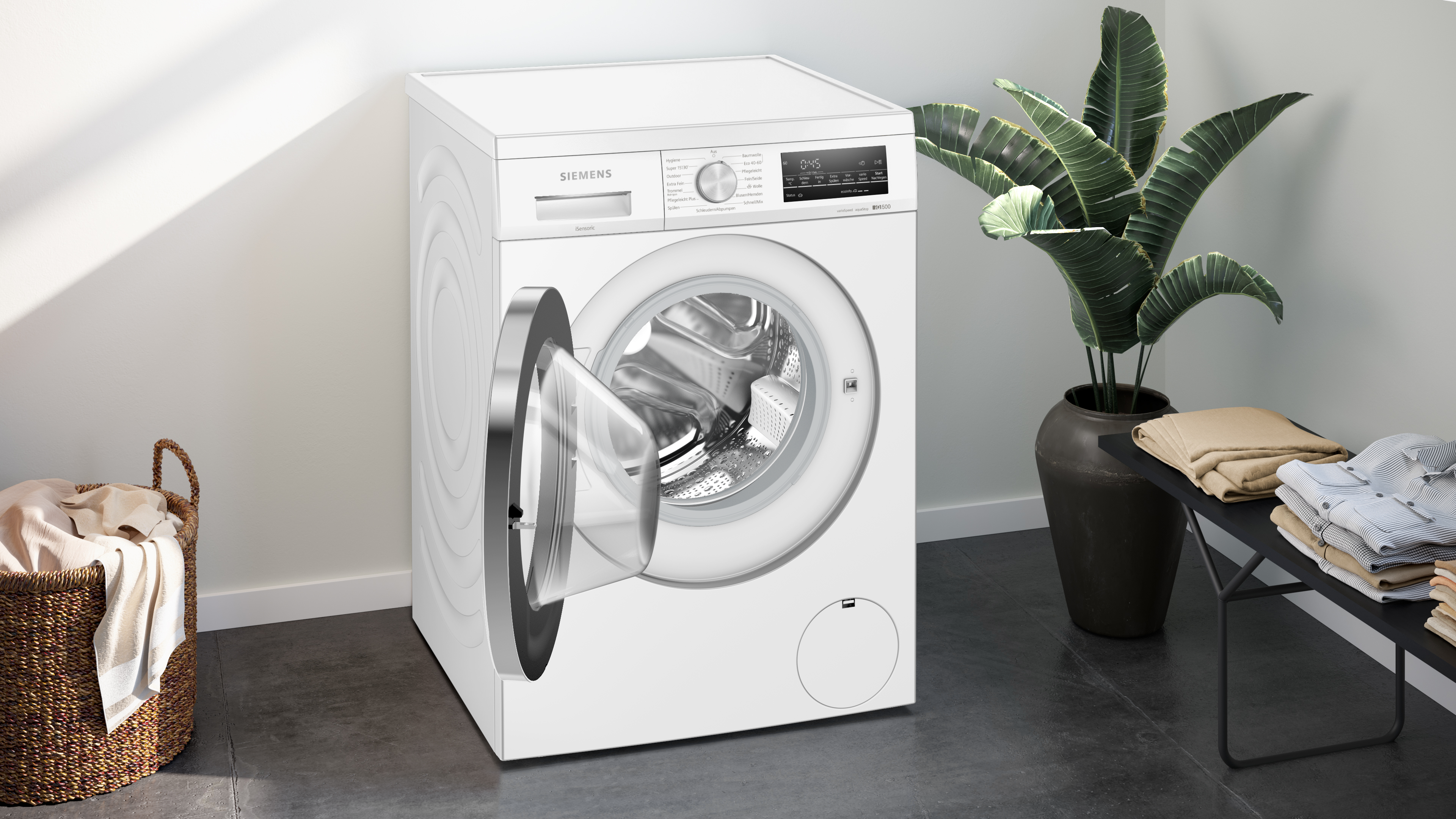 Eine weiße Siemens Waschmaschine mit offener Tür. Kleidung und ein Wäschekorb sind in der Nähe.