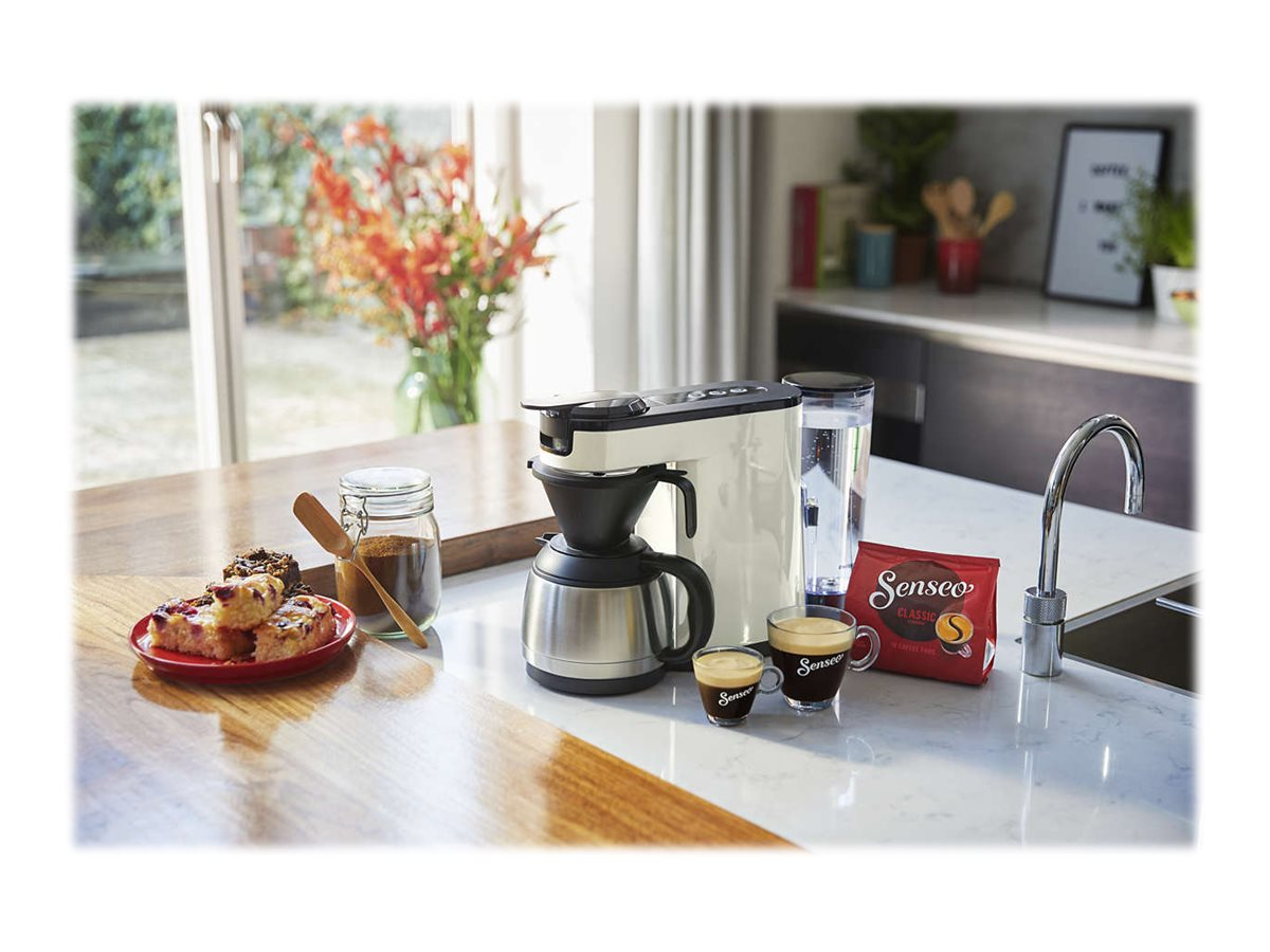 Kaffeemaschine mit Kaffee, Gebäck und Kaffeebohnen auf Holzoberfläche, Küchenhintergrund.