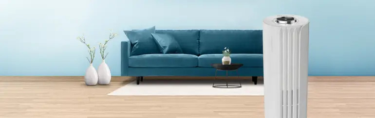 Een witte luchtreiniger naast een blauwe bank in een woonkamer.