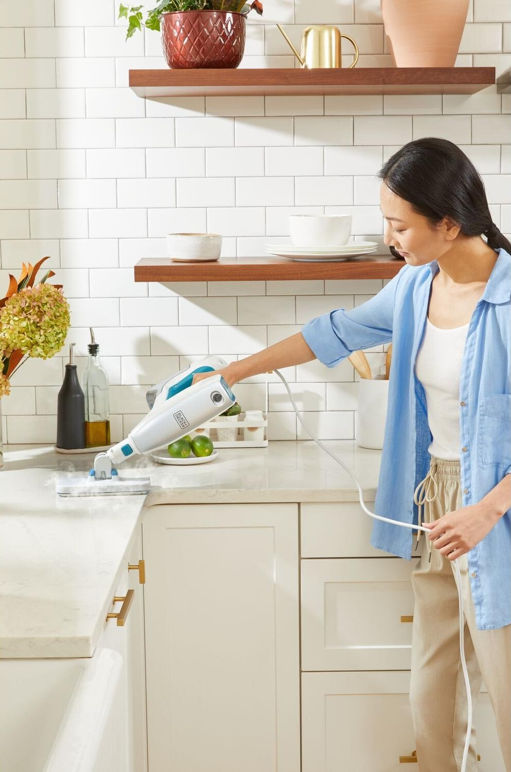 Une femme nettoyant une surface de cuisine avec un nettoyeur vapeur, près d'une fenêtre.