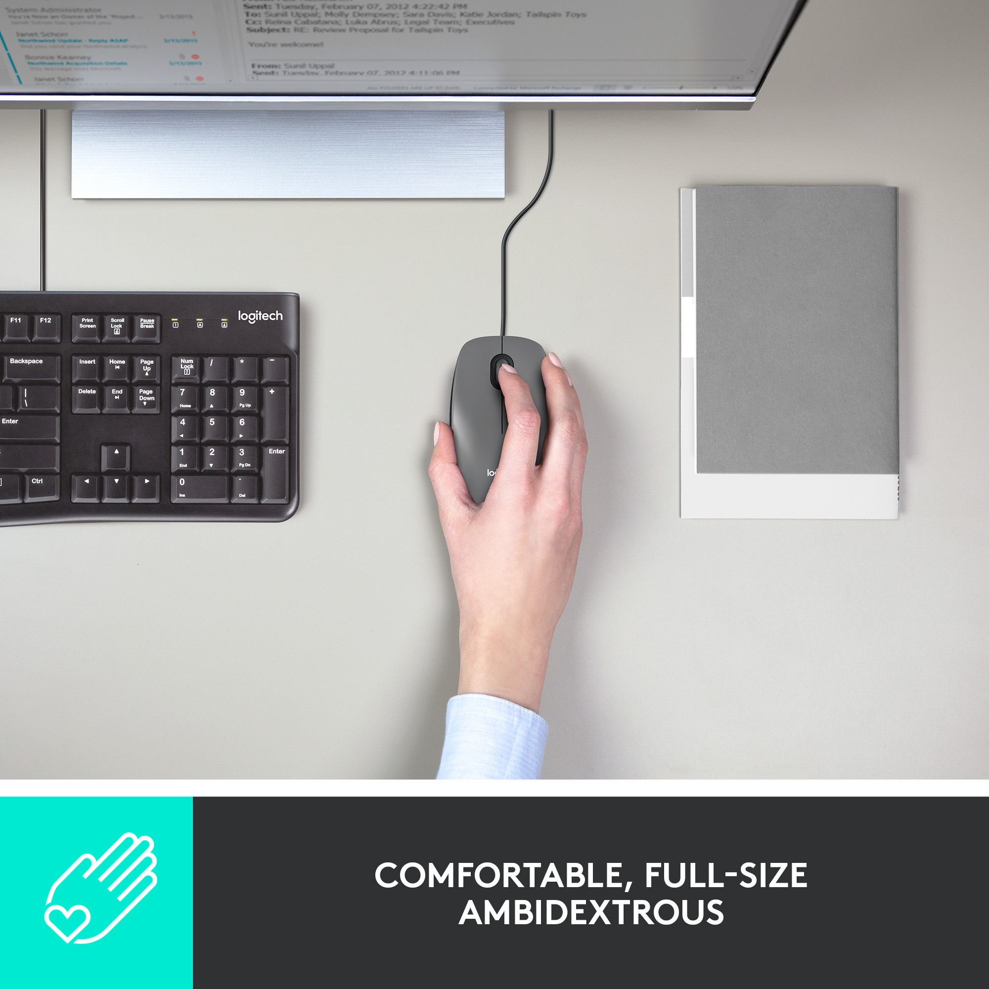 Eine Hand hält eine graue Logitech-Maus neben einer Tastatur und einem Computermonitor.