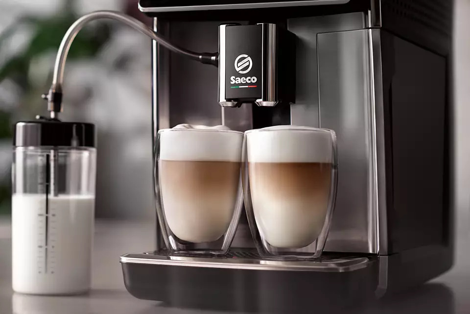 Koffiemachine met twee glazen gevuld met gelaagde latte. Melkcontainer op de achtergrond.