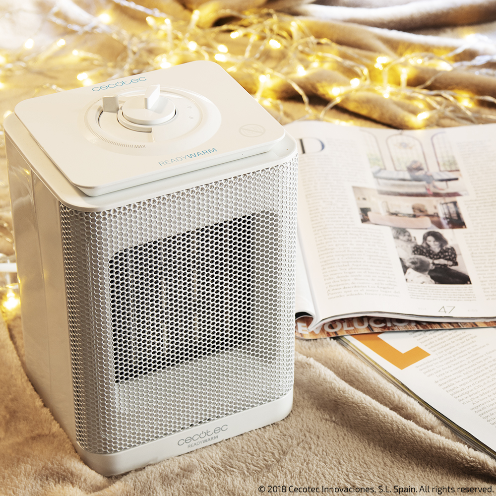 Un calefactor blanco sobre una superficie beige con una revista y luces de hadas.