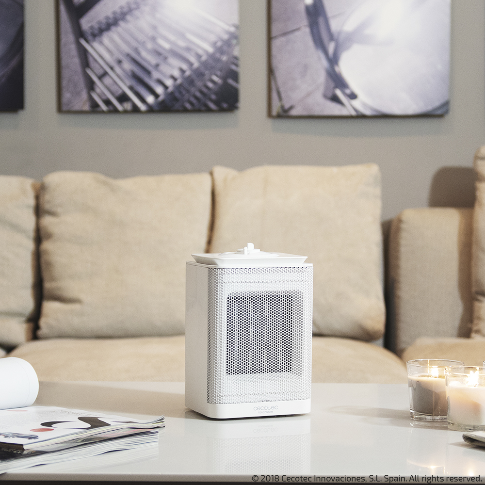 Calentador blanco en una mesa, con velas y sofá en el fondo.