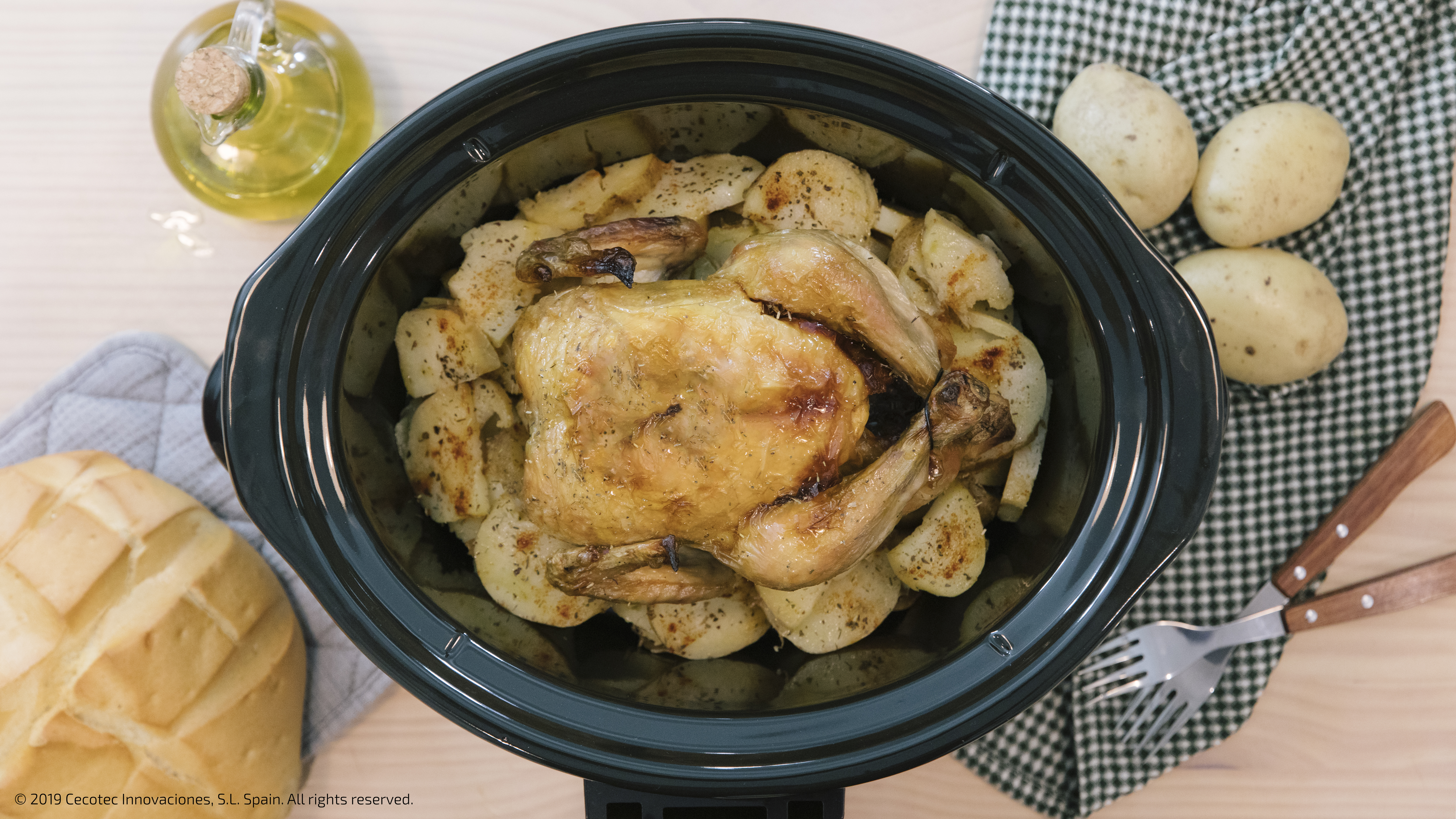 Un pollo asado en una olla negra con patatas y aceite. El entorno es una mesa.