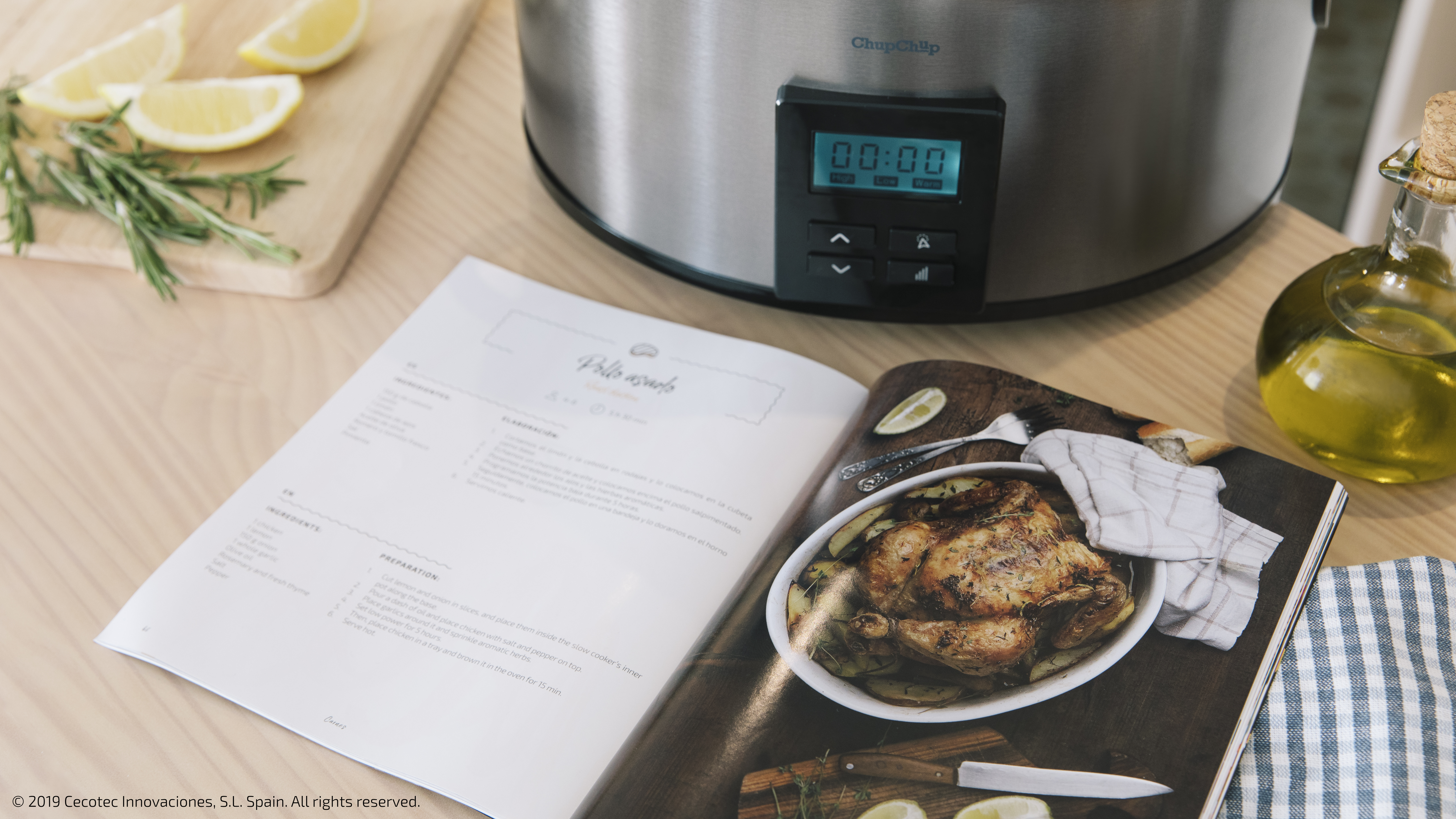 Un libro de cocina abierto sobre una mesa. Junto a él hay limones, romero y una olla de cocción lenta.