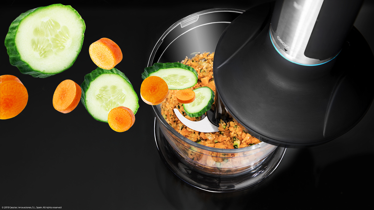 Un procesador de alimentos corta verduras: pepino y zanahorias sobre fondo negro.