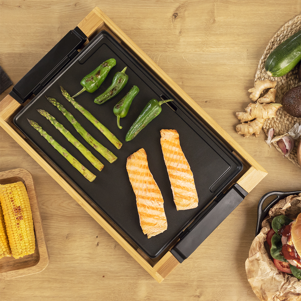 Comida en una parrilla de madera con espárragos, pimientos y salmón. También hay maíz y una hamburguesa.