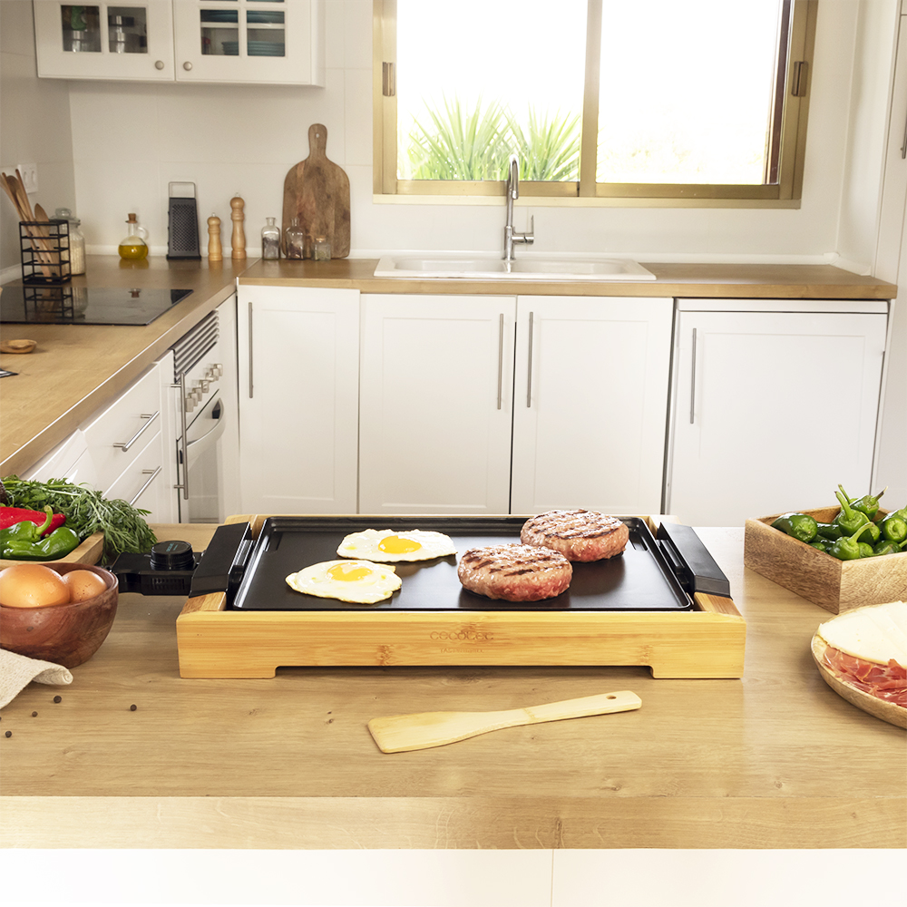 Plancha con huevos y hamburguesas en mesa madera.