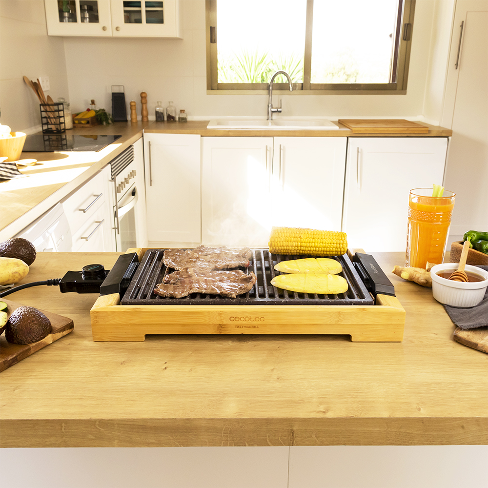 Una parrilla con carne y maíz está sobre una mesa de madera. Un vaso de zumo de naranja está a la derecha.