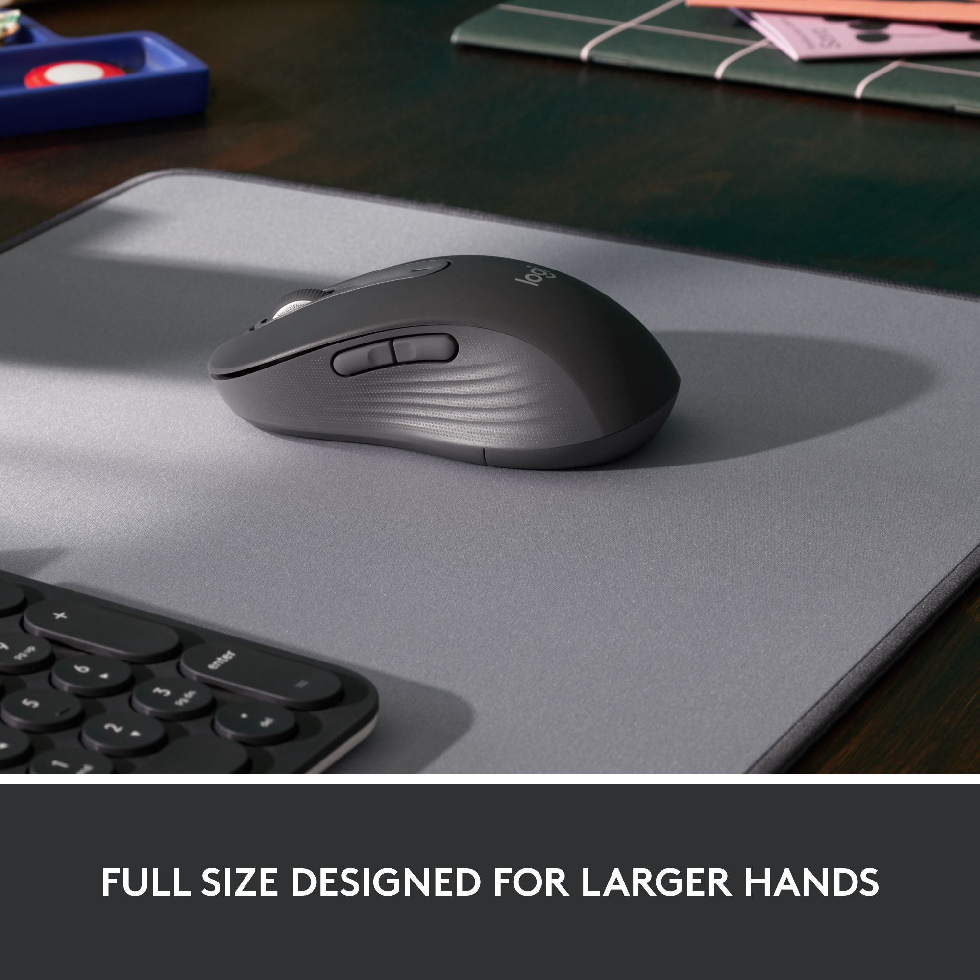 Une souris gris foncé sur un tapis de souris gris, avec un clavier visible en arrière-plan.