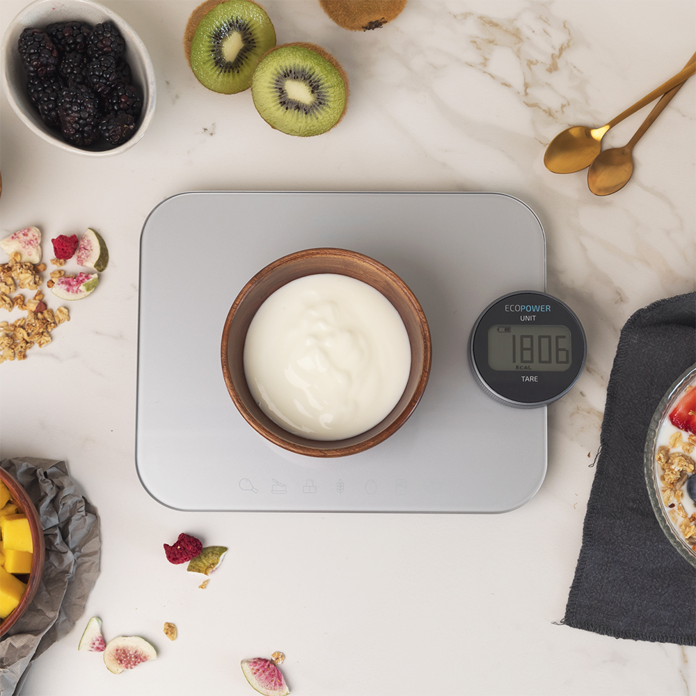 Yogur en un cuenco de madera sobre una báscula con kiwis y bayas. Báscula a la derecha.