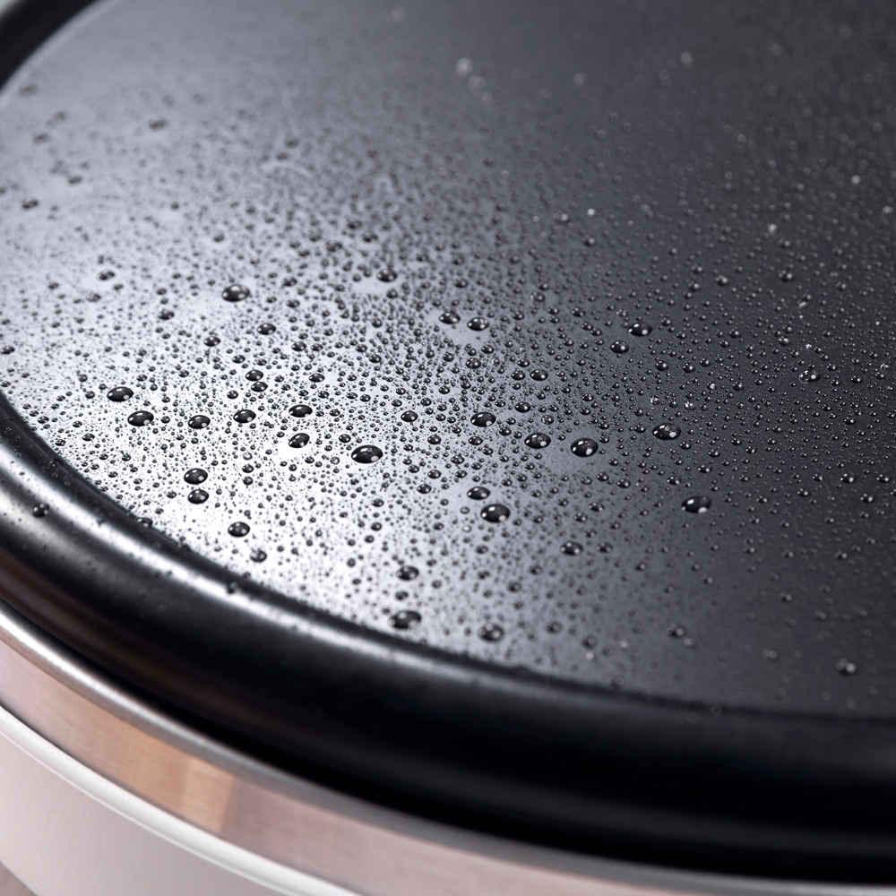 Primer plano de una superficie de plancha negra y circular con muchas gotas de agua.