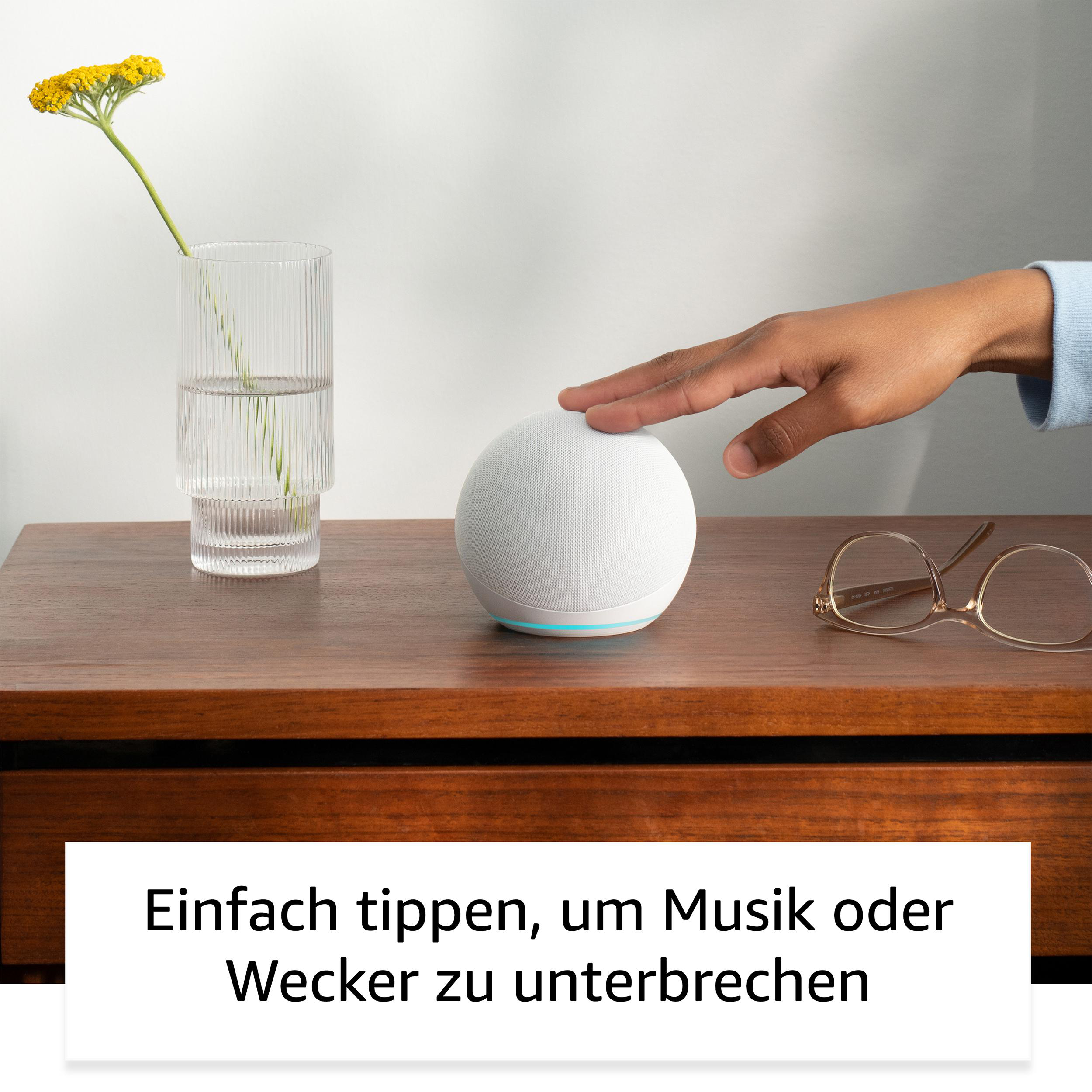 Eine Hand berührt einen weißen intelligenten Lautsprecher auf einem Holztisch, mit einem Glas Blumen und Brillen.