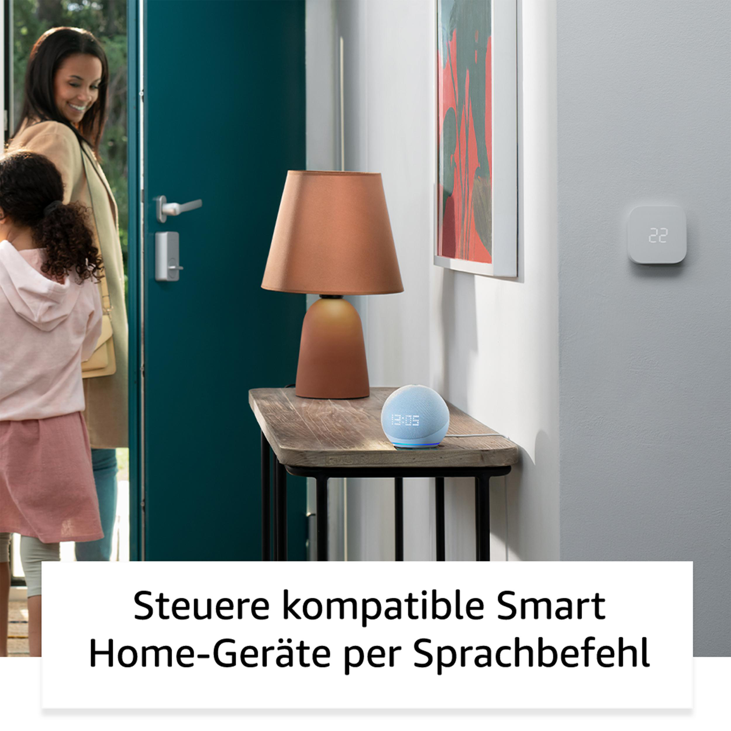 Smart-Lautsprecher auf einem Tisch, Frau und Kind im Hintergrund.
