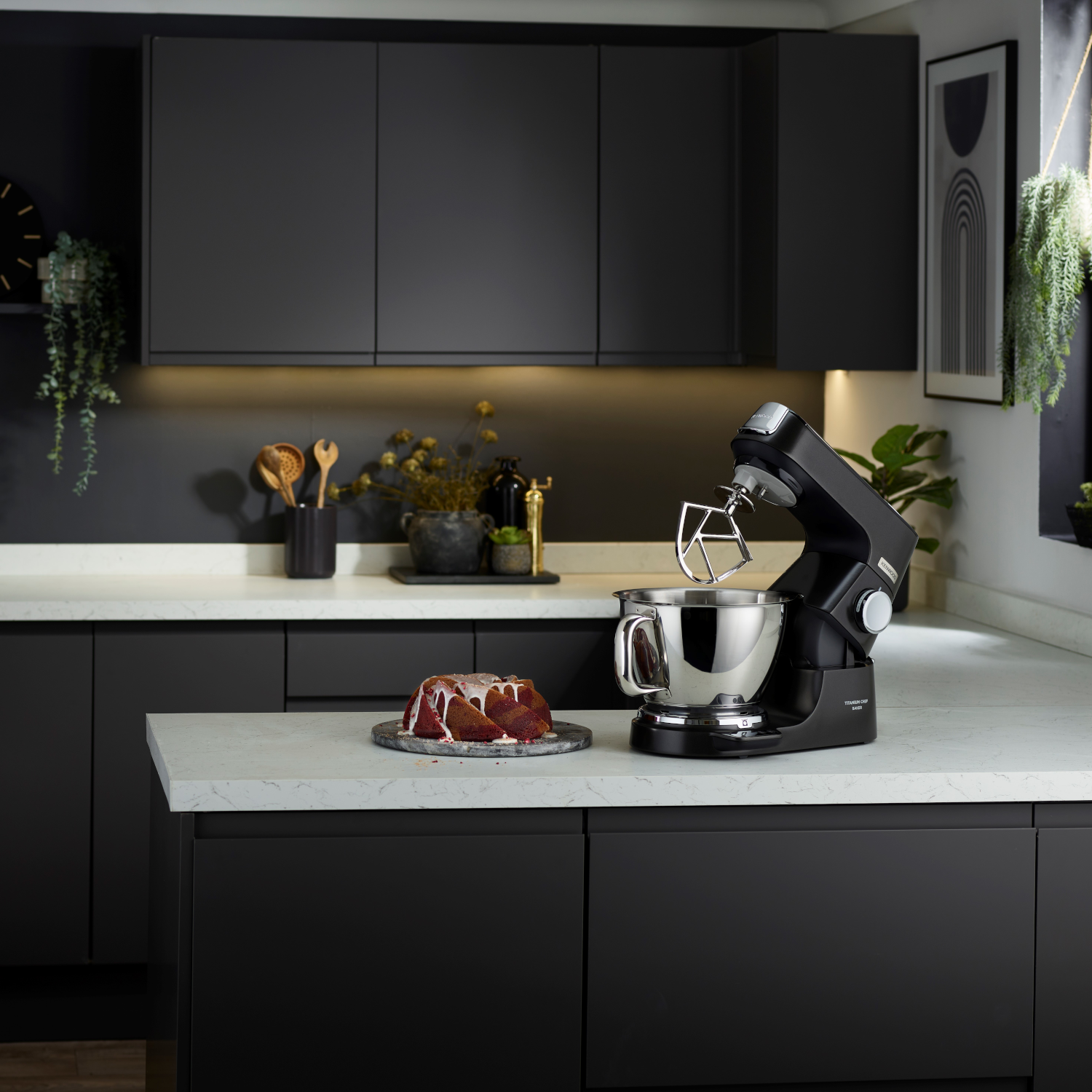Modern kitchen with black cabinets, white countertop, and a stand mixer. A cake is on the counter.