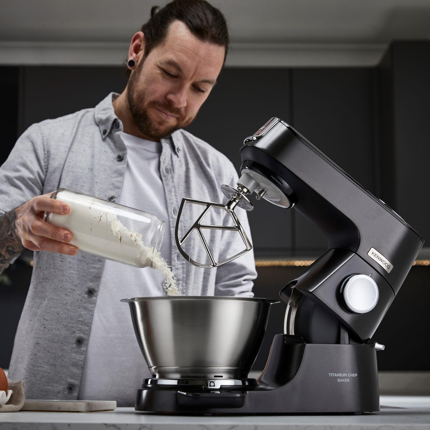 Man pouring flour into a black stand mixer bowl. Kitchen setting.