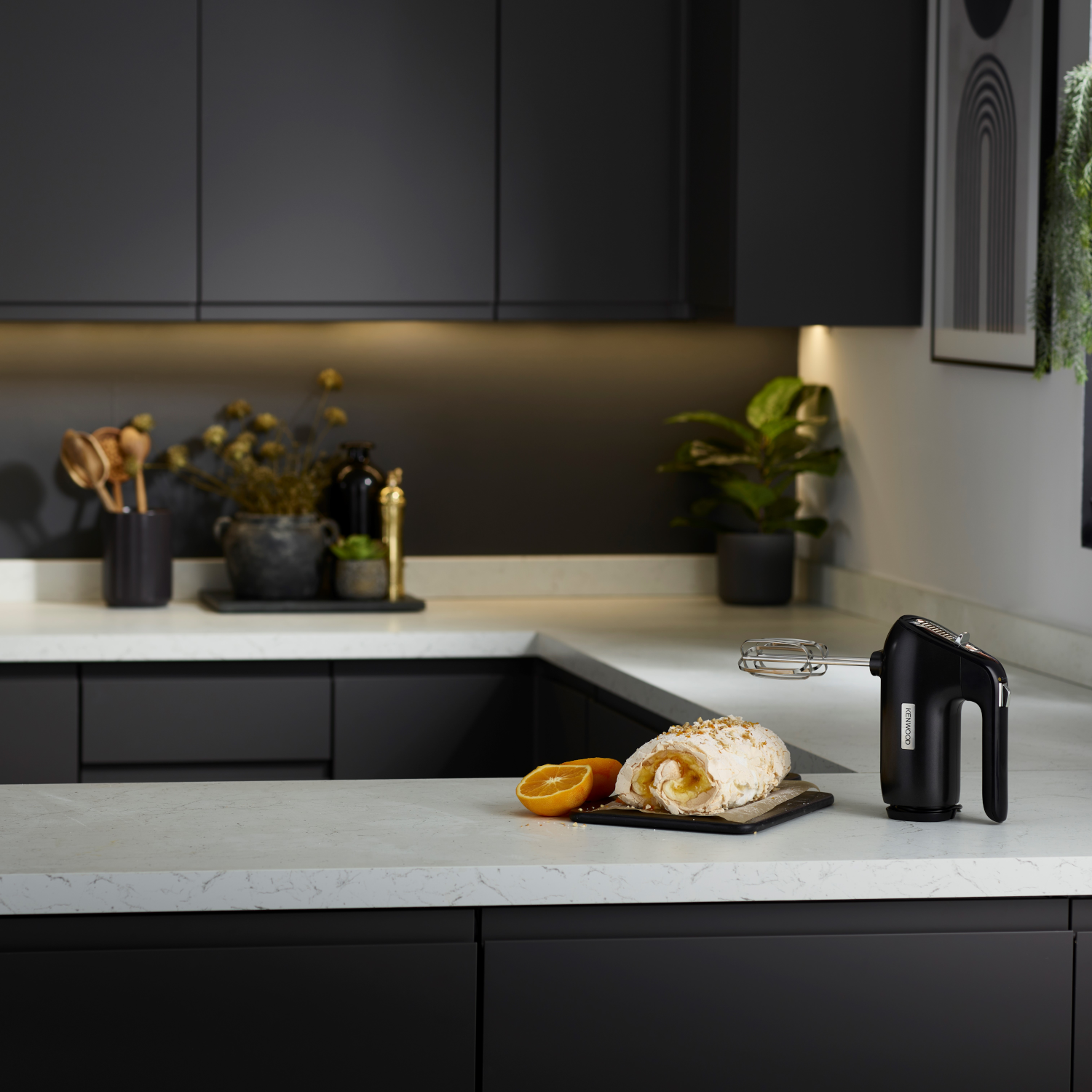 Black hand mixer on a white counter in a kitchen setting. Baked goods are present.