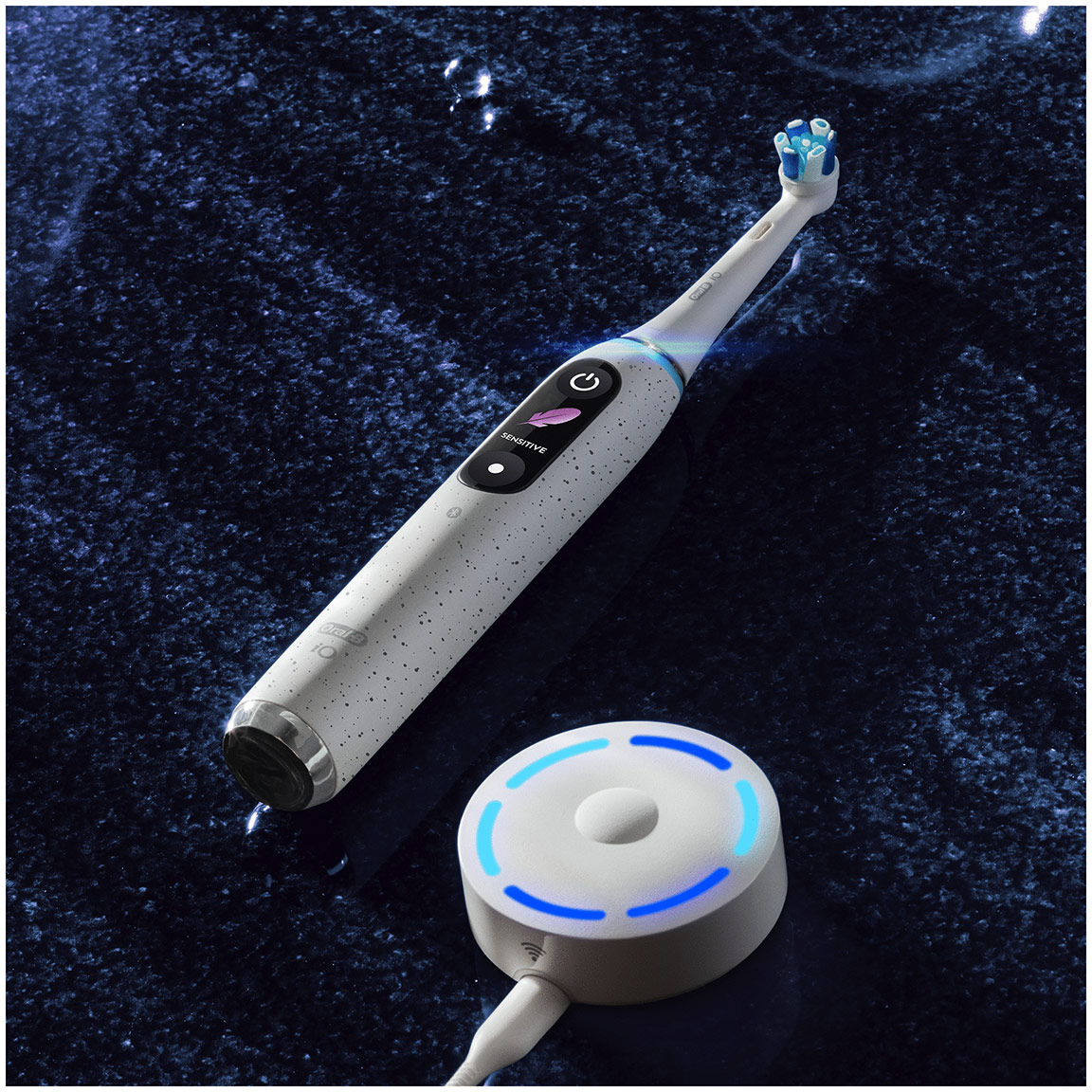 Brosse à dents électrique blanche et argentée avec socle de chargement et lumière bleue.