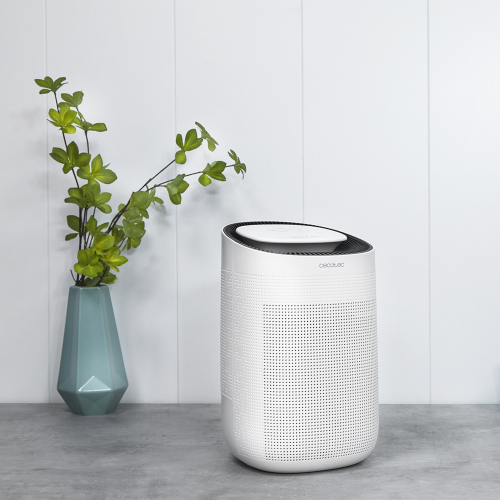 Un humidificador blanco con una planta verde en un jarrón verde azulado. La escena está frente a una pared blanca.