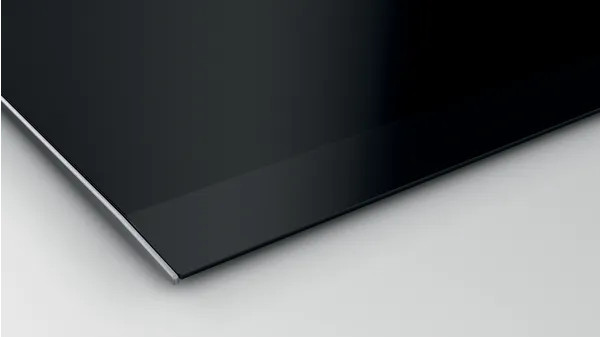A black, glossy, and sleek stovetop with a thin silver edge, shown from an angle.
