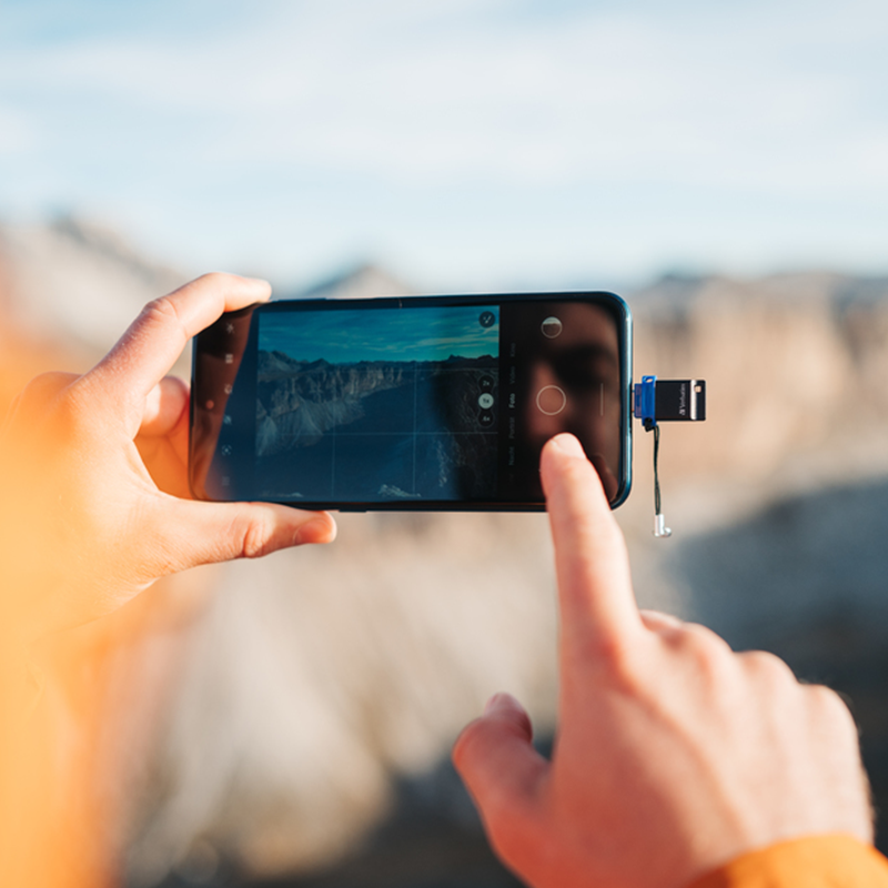 Bir kişi, bir kanyon manzarasının fotoğrafını çekmek için bir akıllı telefon tutuyor.