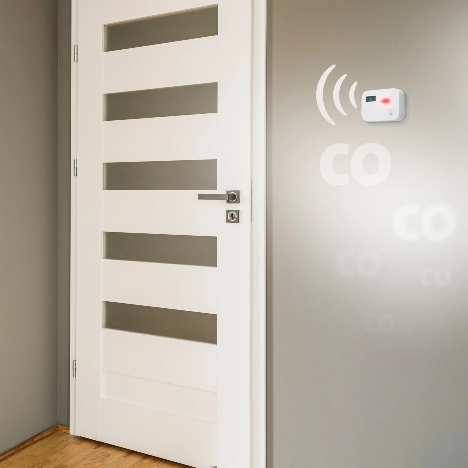 A white CO detector on a gray wall next to a white door. It has a red light.