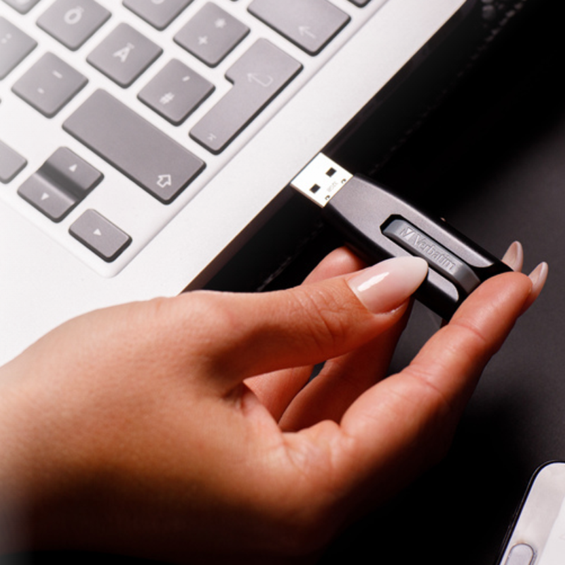 Bir kadın dizüstü bilgisayarın yanında siyah bir USB sürücü tutuyor.
