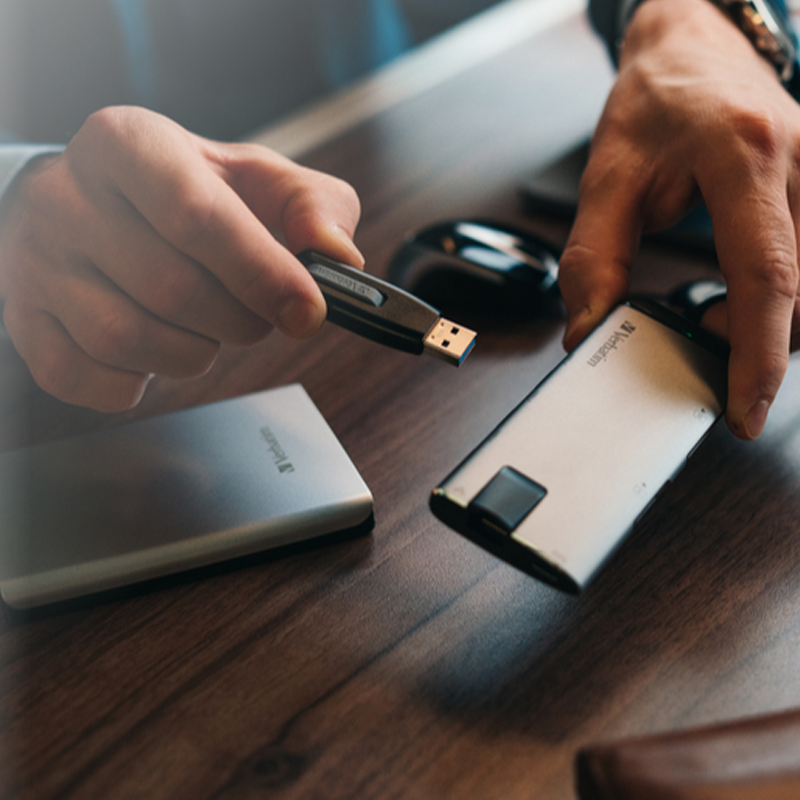 Ahşap bir masa üzerinde bir USB sürücü ve harici bir sabit disk tutan eller.