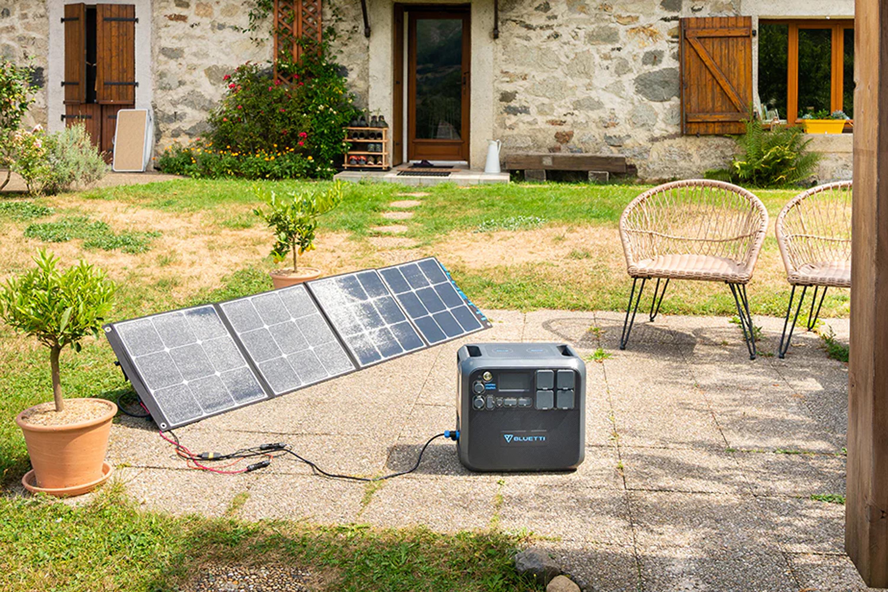 Solarpaneele sind im Garten an eine Stromstation angeschlossen. Haus und Stühle im Hintergrund.